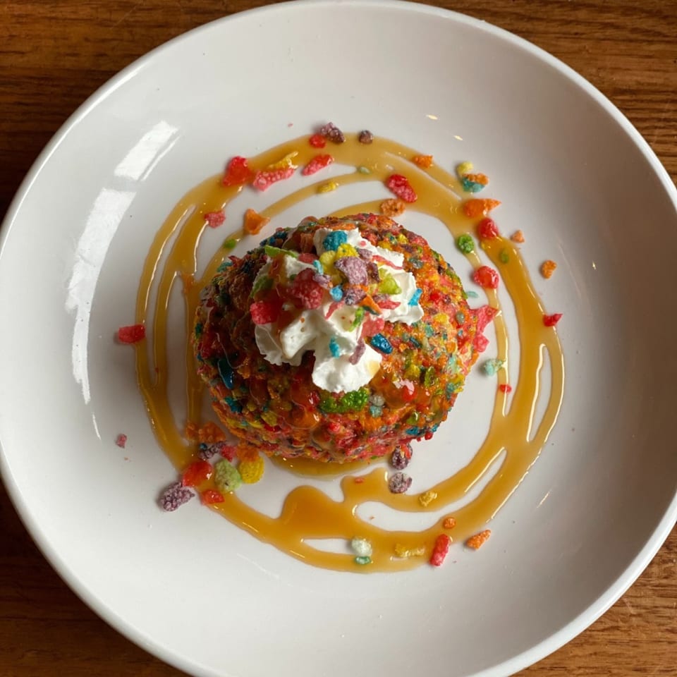 Colorful dessert ball covered in fruity cereal, topped with whipped cream and caramel drizzle.